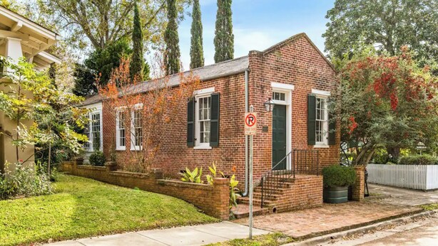 A small brick house with a green door, white shutters, and a no parking sign.