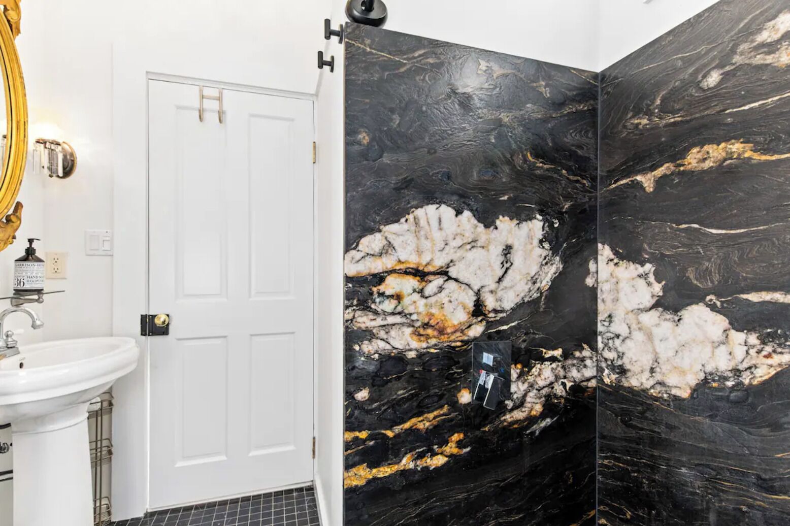 A bathroom with a white sink, a door, and black marble walls with gold veins.