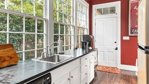 A kitchen with a large window, white cabinets, a stainless steel sink, and a refrigerator.