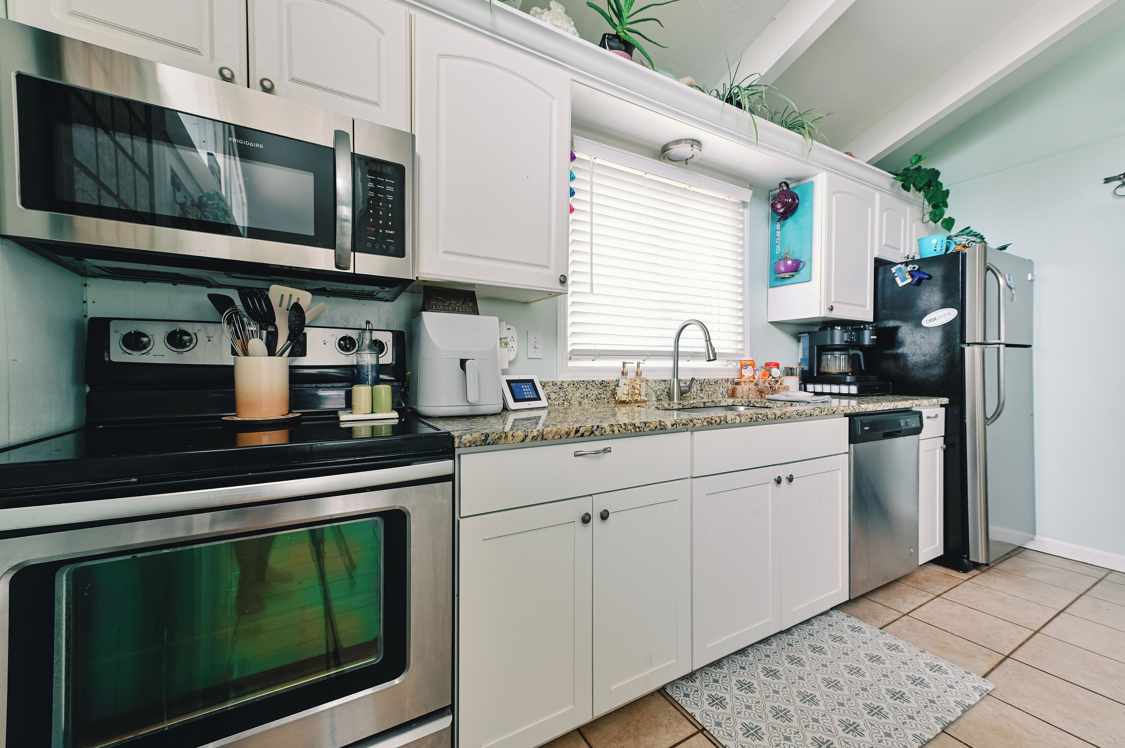 A modern kitchen with stainless steel appliances, white cabinetry, and a granite countertop.