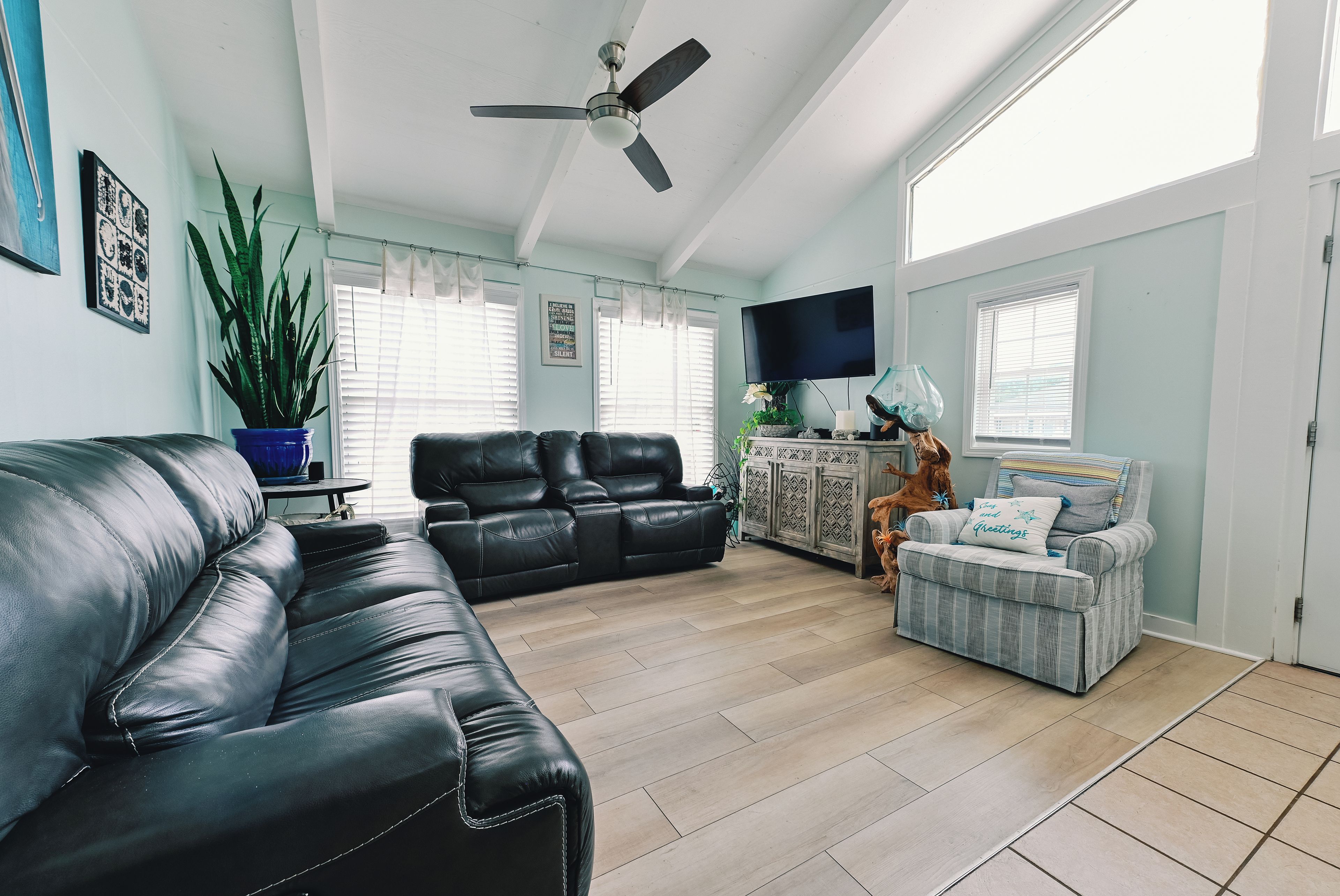A living room with a black leather sofa, a grey striped armchair, a wooden cabinet, and a television on the wall.