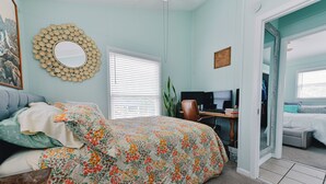 Une chambre à coucher comprenant un lit, un bureau, un ordinateur et une porte donnant sur une autre pièce.