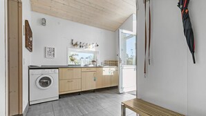 Une cuisine moderne dotée d’un lave-linge encastré, de meubles en bois et d’une grande fenêtre laissant entrer la lumière naturelle.