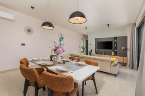 A modern dining area with a white table, brown chairs, and pendant lighting.