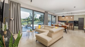 A modern living room with a beige sofa, a dining area with a table and chairs, and a kitchen with a refrigerator and pendant lights. - Villa Benina Rossa Inn (Istria - Žminj) (Žminj)