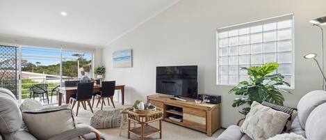 Een moderne woonkamer met een televisie, bank en eethoek.