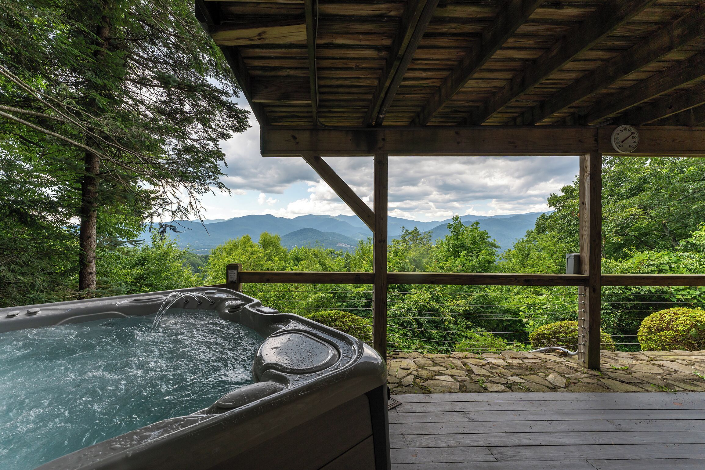 Un bain à remous sous une pergola en bois, avec vue sur les montagnes et la verdure.