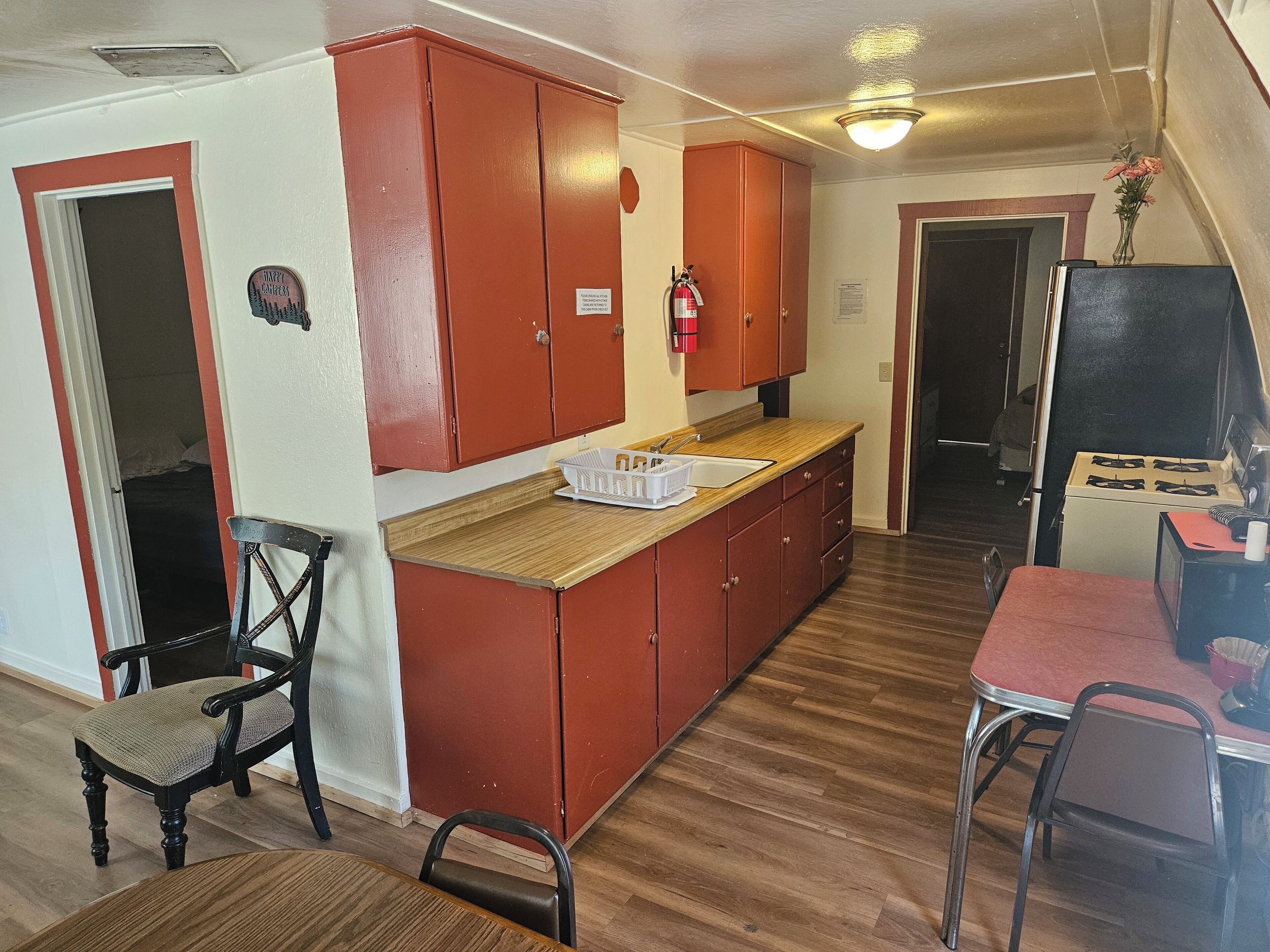 A compact kitchen with wooden cabinets, a sink, and a stove. There is a chair and a dining table with chairs.