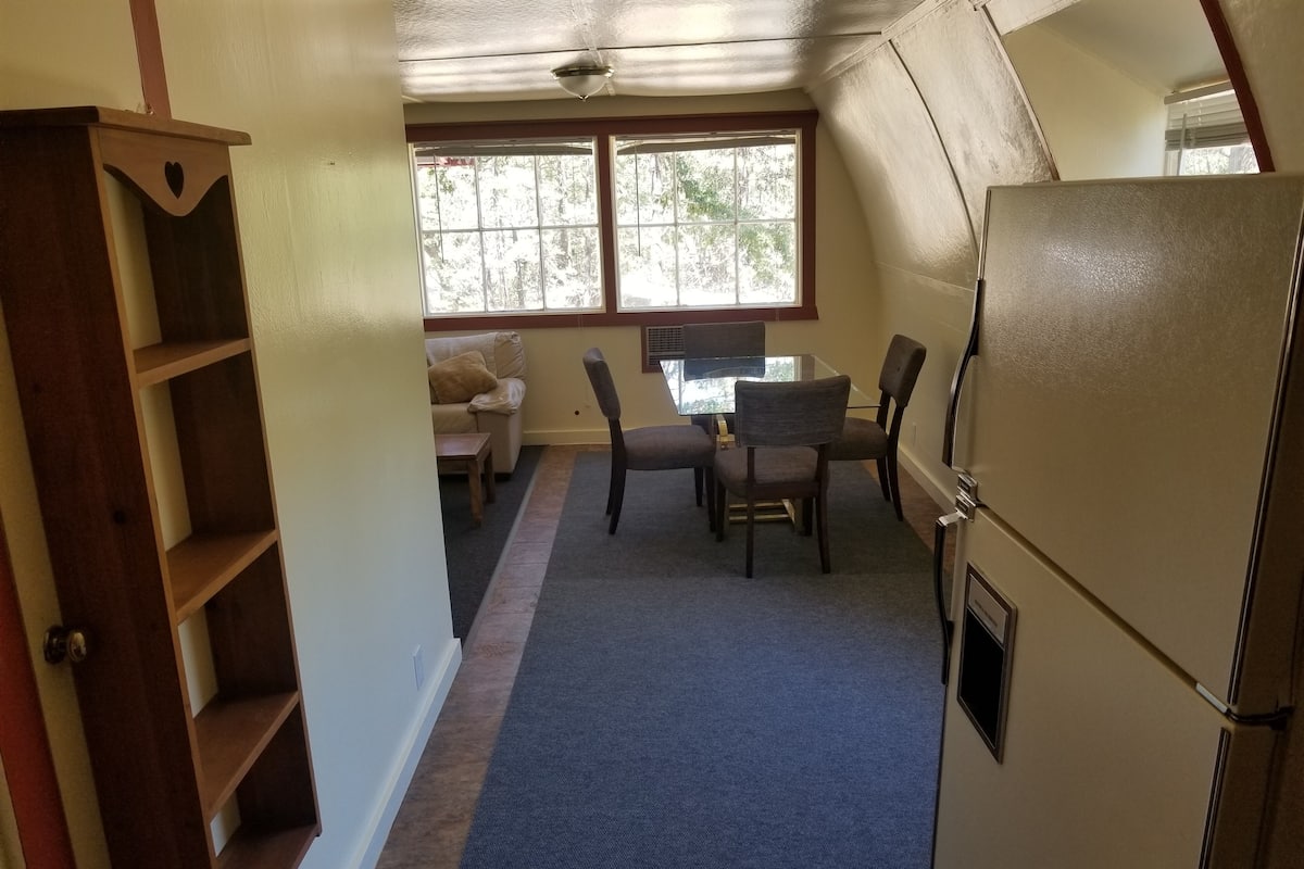A compact kitchen with a refrigerator, a dining table with chairs, and a window providing natural light.