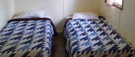 A small, simple room with two beds, plain walls, and a window with curtains.