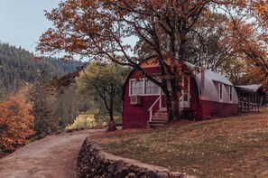 En rustik stuga med en veranda, omgiven av höstlövens färgprakt och en skog i bakgrunden.
