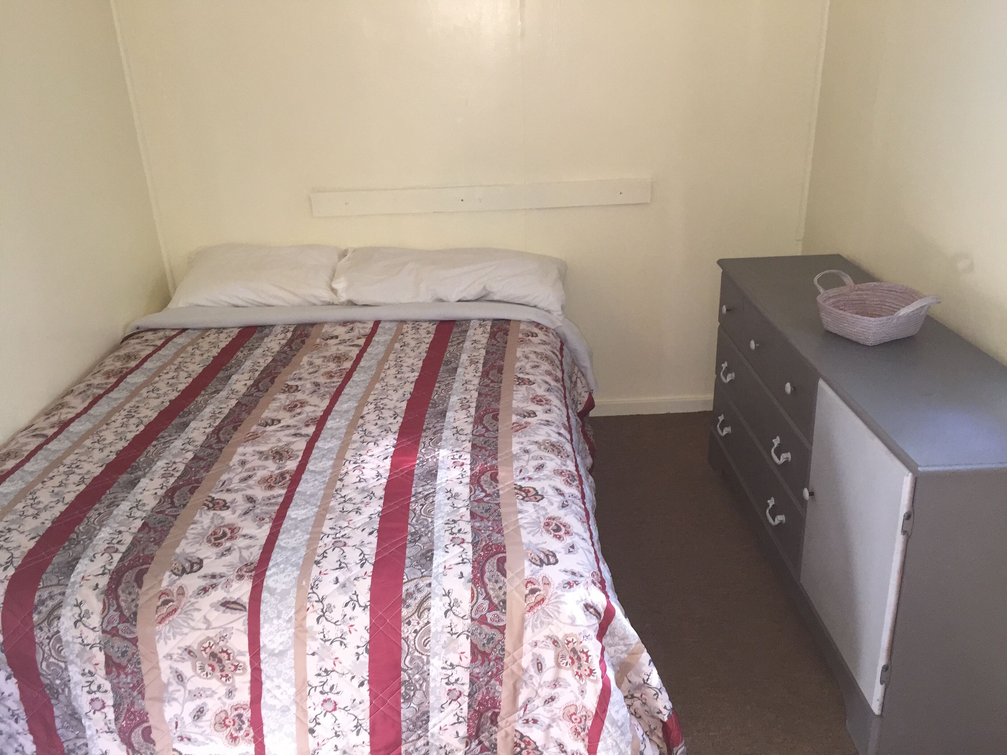 Un dormitorio con una cama, un aparador y una cesta encima de este.