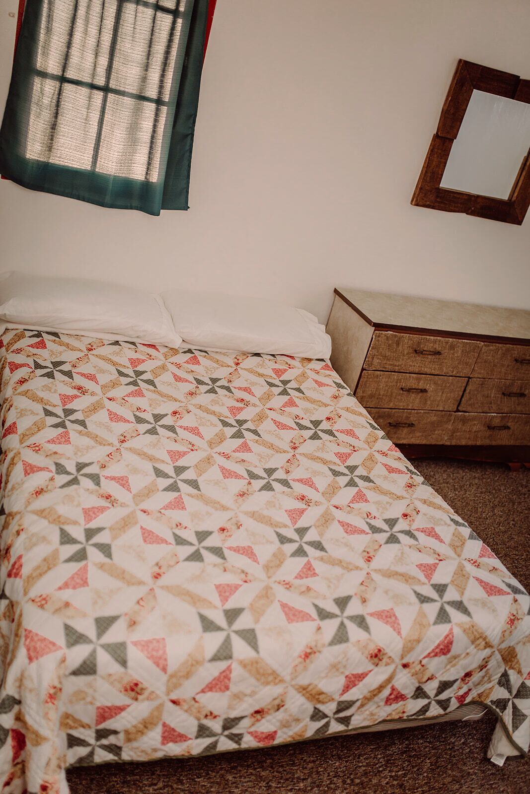 A bedroom with a bed, a dresser, a mirror, and a window with curtains.