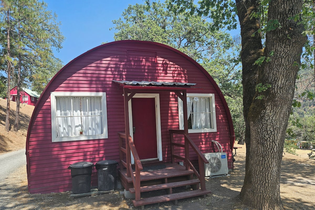 A small, red, dome-shaped cabin with a wooden porch and two windows.