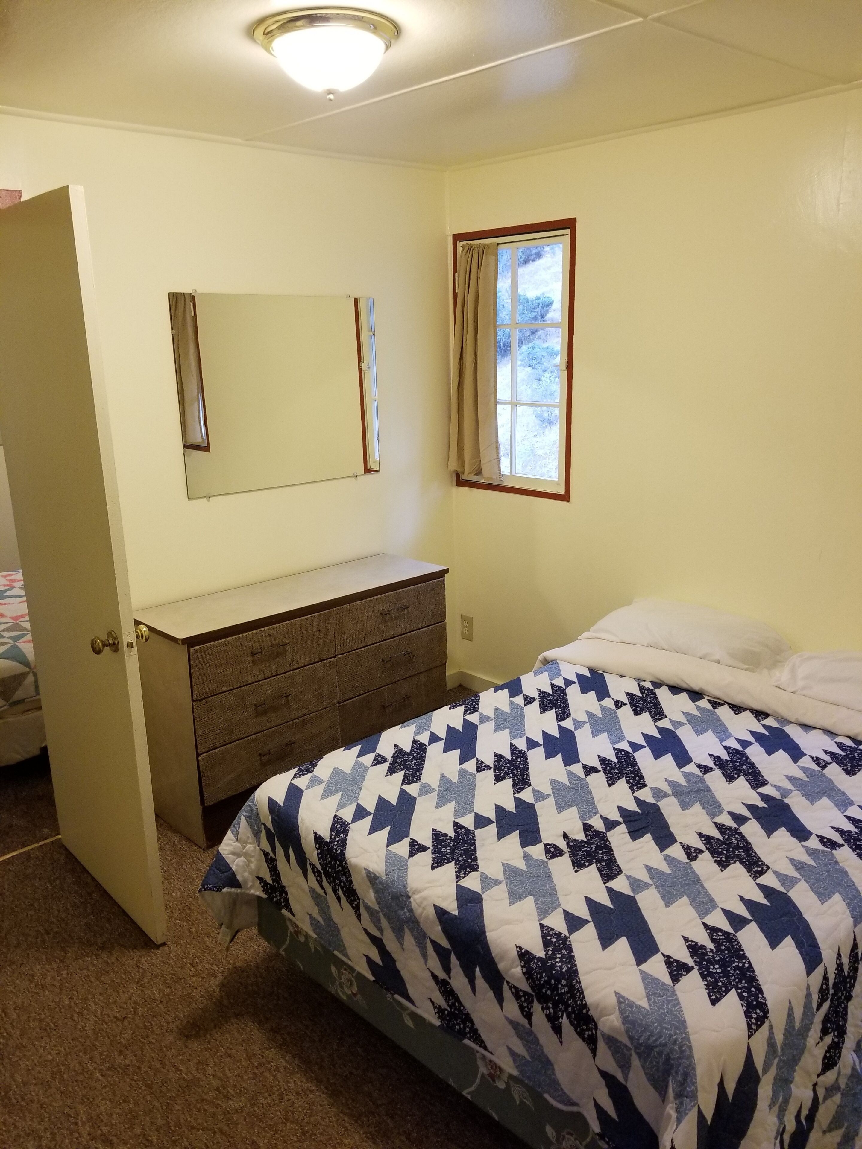 Un dormitorio con cama, cómoda, espejo y ventana con cortinas.