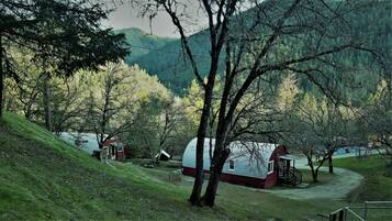 Una cabaña rústica con techo rojo y paredes blancas, rodeada de árboles y un lago.