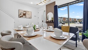 Une salle à manger moderne avec une grande table dressée pour six personnes, entourée de chaises contemporaines.