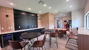A modern kitchen with wooden cabinets, a black refrigerator, and a dining area with round tables and chairs.