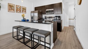 Une cuisine moderne dotée d’un îlot central, de tabourets de bar, d’appareils électroménagers en acier inoxydable et d’un four à micro-ondes placé au-dessus de l’îlot.
