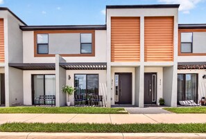 A modern townhouse with a flat roof, large windows, and a small patio area with outdoor seating.