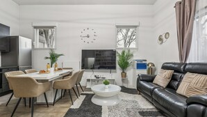 Een moderne woonkamer met een eethoek, een zwarte leren bank, een ronde salontafel en een flatscreen televisie.