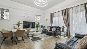 Een moderne woonkamer met een eethoek, een zwarte leren bank, een televisie en een klok aan de muur.