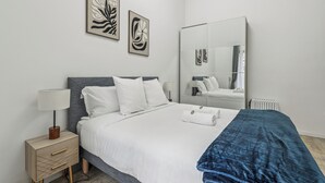 Een moderne hotelkamer met een bed, nachtkastje, lamp en een kunstwerk aan de muur.