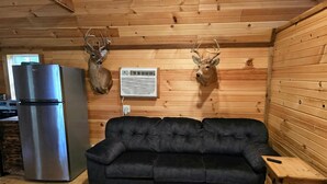 L’intérieur d’une cabane avec un canapé noir, un réfrigérateur en acier inoxydable et deux têtes de cerf fixées au mur.