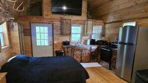 Une cabane comprenant un lit, une cuisine avec un réfrigérateur et un téléviseur fixé au mur.