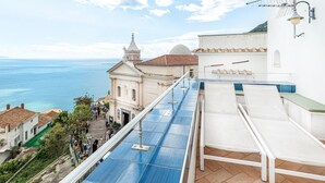 A rooftop terrace with blue solar panels, a white building with a dome, and a view of the sea.