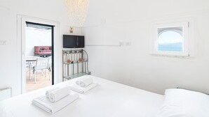 A hotel room with a bed, a TV mounted on the wall, a small window, and a balcony with outdoor furniture.