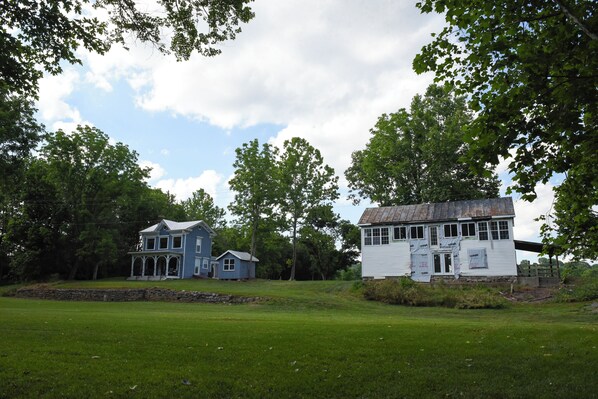 A large, two-story house with a porch and a smaller attached structure, surrounded by a grassy field and trees. - Farmhouse on the river! (Timberville)