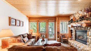 A cozy cabin interior with a stone fireplace, wooden ceiling, and a large window overlooking greenery. - World-class Ski spot + Year-round Pool & Hot Tub! (Park City)