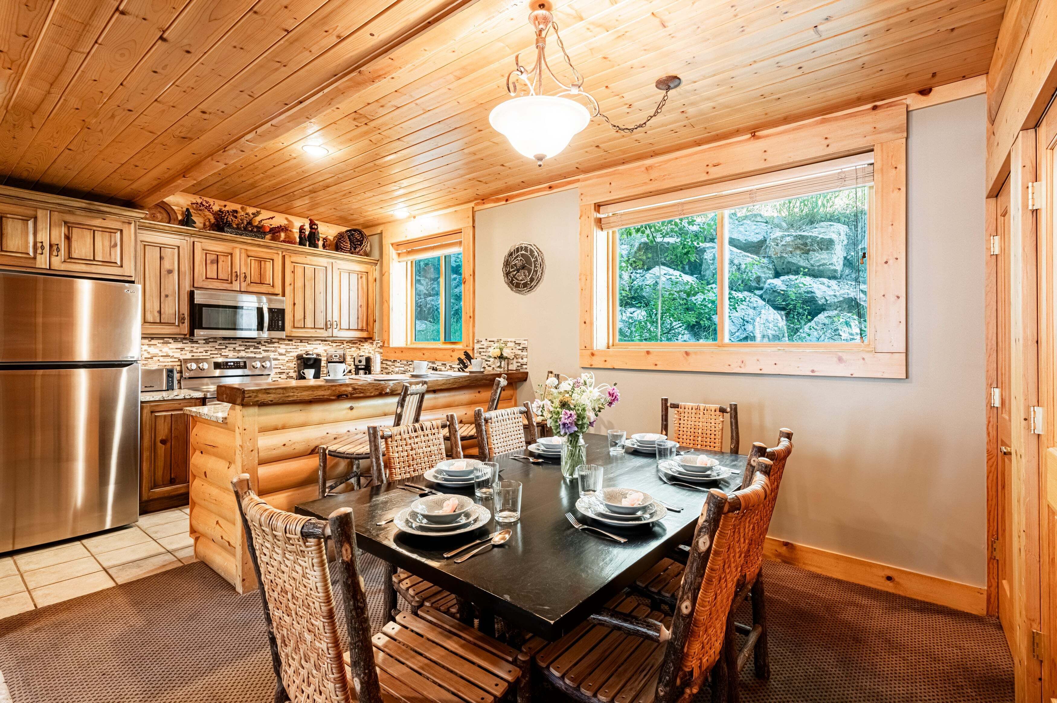 A wooden cabin interior with a kitchen, dining table, and log fireplace.