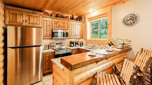 A log cabin kitchen with wooden cabinets, stainless steel appliances, a stone backsplash, and a wooden island with seating. - World-class Ski spot + Year-round Pool & Hot Tub! (Park City)