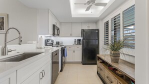 A modern kitchen with white cabinets, a black refrigerator, a microwave, and a ceiling fan. - 2/2 Corner Unit Condo in Bonita Bay! Large Lanai Space! (Bonita Springs)