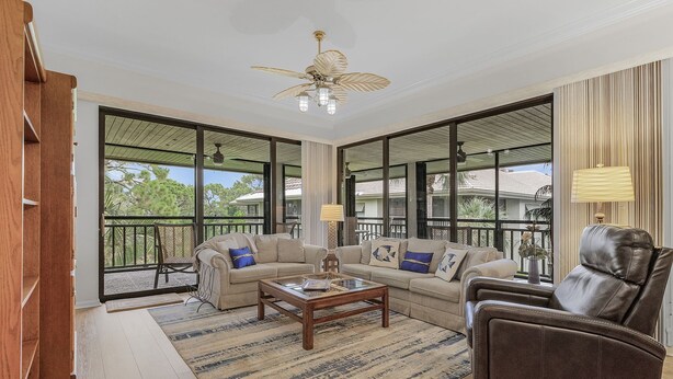 A spacious living room with a large window, a ceiling fan, and a leather armchair. - 2/2 Corner Unit Condo in Bonita Bay! Large Lanai Space! (Bonita Springs)