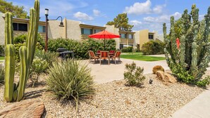 Une cour avec une table et des chaises, entourée de cactus et de plantes du désert.
