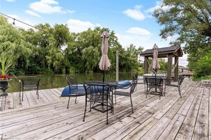 Una terraza de madera con mobiliario exterior, incluyendo sillas y una mesa, con vista a un cuerpo de agua.