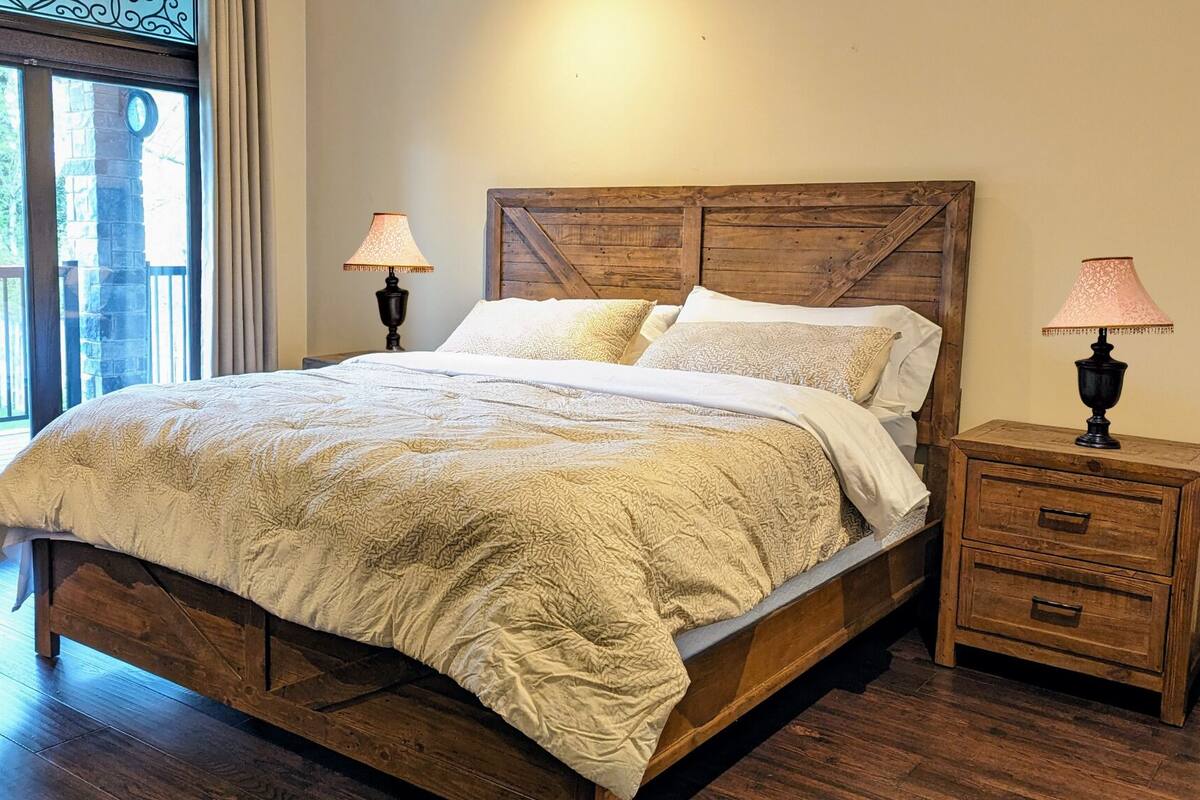 A wooden bed with a quilted bedspread, two bedside lamps, and a wooden nightstand with drawers.
