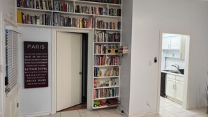Een kamer met een boekenplank vol boeken, een deur met een bord waarop bezienswaardigheden van Parijs staan vermeld, en een keuken met kastjes en een gootsteen.