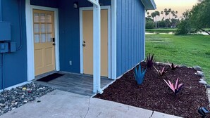 Een blauw huis met een voordeur, een overdekte veranda en een tuin met planten.