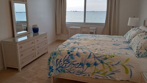 Ein Schlafzimmer mit Bett, Schminktisch, Spiegel, Fenster mit Meerblick und Schreibtisch mit Stuhl.
