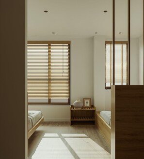 Une chambre à coucher au style minimaliste, avec un lit en bois, une table de chevet dotée d’une lampe et une grande fenêtre équipée de stores.