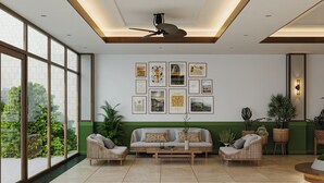 Una sala moderna con un sofá, dos sillones, una mesita de centro y un ventilador de techo. La habitación cuenta con ventanas amplias, una pared de acento verde y obras de arte enmarcadas.