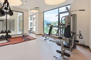 Una palestra con attrezzature per esercizi, uno specchio e vista su un paesaggio montuoso attraverso ampie finestre.