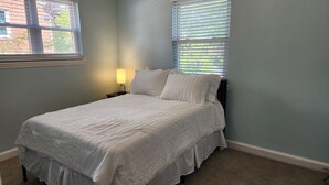 A neatly made bed with a white bedspread and pillows, a bedside lamp, and a window with blinds. - Convenient/family friendly home with yard driveway

 (Silver Spring)
