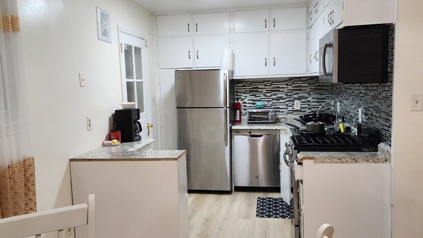 A compact kitchen with white cabinets, a stainless steel refrigerator, a microwave, and a dishwasher. - Convenient/family friendly home with yard driveway

 (Silver Spring)
