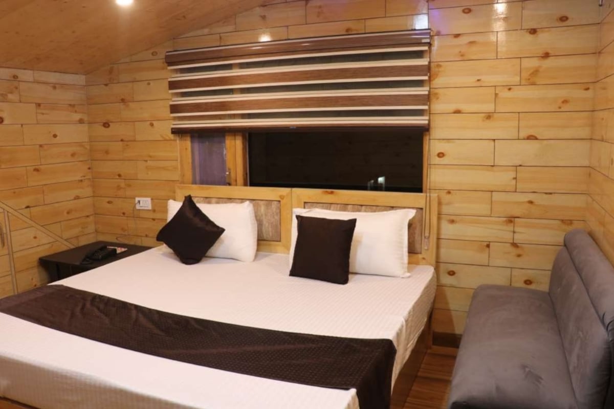 A wooden cabin bedroom with a bed, pillows, a window, and a sofa.