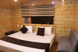 Une chambre dans une cabane en bois, avec un lit, des oreillers, une fenêtre et un canapé.